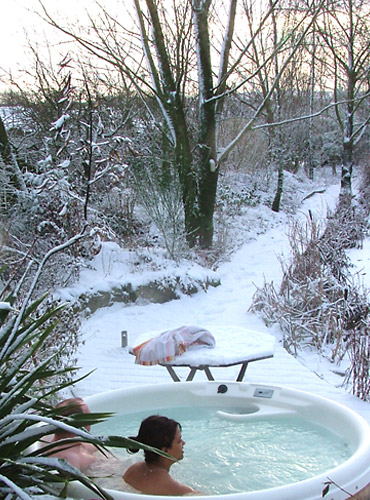 A couple sit in the hot tub in winter surrounded by snowy landscape.